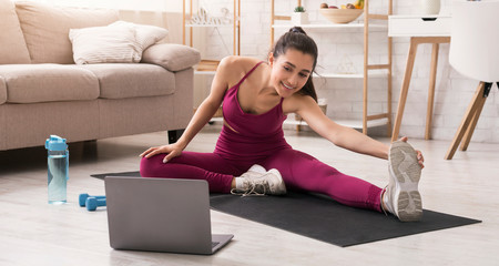 Stay active during self isolation. Lovely girl stretching and watching video on laptop at home. Panorama