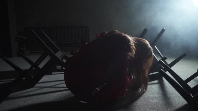 Girl in a red straitjacket in a psychiatric clinic sits on the floor among the chairs around