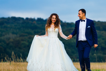 happy newlyweds hold hands and walk near the forest