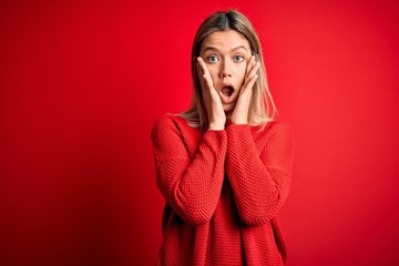 Young beautiful blonde woman wearing casual sweater over red isolated background afraid and shocked, surprise and amazed expression with hands on face