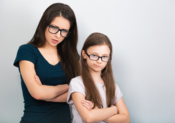 Serious thinking mother and sad doubt kid in glasses with folded arms on light blue background. Closeup studio portrait. Online education. Distance learning.
