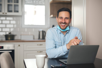 Portrait of a businessman working from home wearing mask around neck.