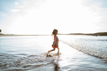 Fototapeta premium Little girl running on the beach while playing water on a beautiful beach
