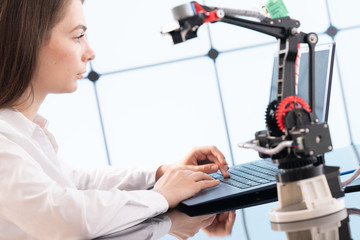 A young woman writes an algorithm for the robot arm. Science Research Laboratory for Robotic Arm Model. Computer Laboratory