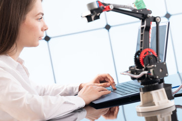 A young woman writes an algorithm for the robot arm. Science Research Laboratory for Robotic Arm...
