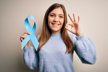 Young blonde woman holding prostate cancer awareness campaing blue ribbon doing ok sign with...