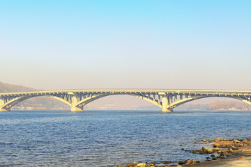 Beautiful spring morning landscape photo of Metro bridge across Dnipro River in Kyiv. The bridge is used for metro and for automobile traffic. Cityscape in the morning smog in the background
