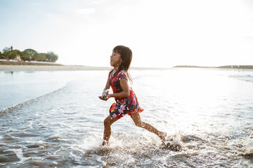 Little girl running on the beach while playing water on a beautiful beach