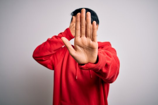 Young beautiful asian girl wearing casual sweatshirt with hoodie over white background covering eyes with hands and doing stop gesture with sad and fear expression. Embarrassed and negative concept.