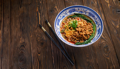 Delicious and spicy homemade sichuan rice noodle in traditional blue bowl with black chopsticks on wooden table, asian food concept copy space for menu design