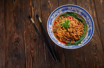 Delicious and spicy homemade sichuan rice noodle in traditional blue bowl with black chopsticks on wooden table, asian food concept copy space for menu design