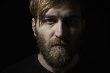 Portrait of a depressed middle aged man in a dark sweater on a dark background.