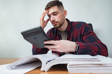 A man with a calculator against the background of many financial documents. Large amount of...