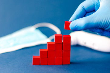 Hand in protective glove adding a red cube to assemble  growing column graph representing a rising...