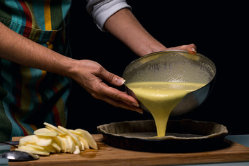 Working in the kitchen. Detail of hands pouring mash prepared in the dough. Cook apple pie.Culinary ingredients. fruit cake. Kitchen table Dark black background.