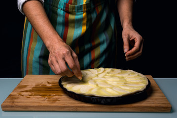 Working in the kitchen. Detail of hands Putting apple pieces on the cake. Preparing to bake. Cook apple pie. fruit cake. Kitchen table Dark black background.