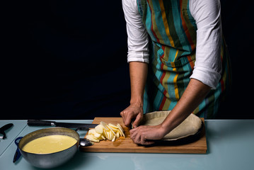 Obraz na płótnie Canvas Working in the kitchen. Detail of hands putting the dough in the mold. Cook apple pie. fruit cake. Kitchen table Dark black background.