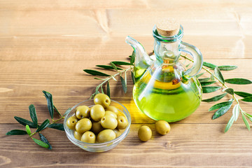 Olive oil in the glass bottle, olives in the bowl and branches of olive tree on the wooden background in the sunlights.