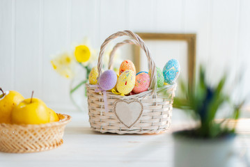 Multi-colored Easter eggs in a basket on a white wooden background
