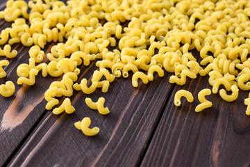 Raw pasta on a dark wooden table, yellow macaroni on a brown wood boards. Traditional Italian cuisine. Food background.