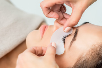 Hands of cosmetologist puts strip under eye of young woman before eyelash extension procedure.