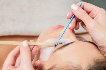 Hand of cosmetologist wipes eye of woman by cotton bud.