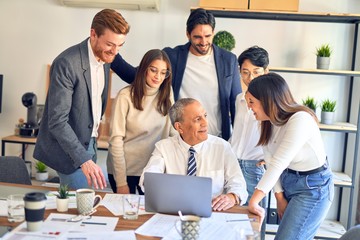Group of business workers smiling happy and confident. One of them sitting and partners standing around. Working together with smile on face looking at the laptop at the office