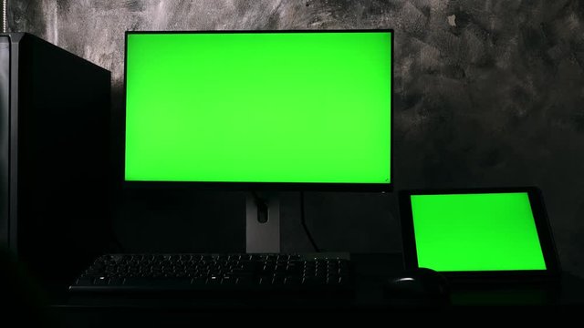 Computer, tablet with green screen monitors on the desk in the dark room at home