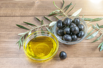 Olives and olive oil  in glass transparent bowl , branches of olive tree on the wooden background...