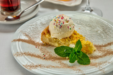 Piece of cake charlotte with apples ice cream ball and fresh mint on white plate. Served with a rosette of honey, a cup of aromatic tea and a glass of white wine