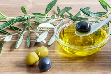 Foto op Plexiglas Olive oil in the glass transparent bowl, spoon with black olive , olive tree branches on the wooden background closeup. Mediterranean healthy diet food. © zveruga