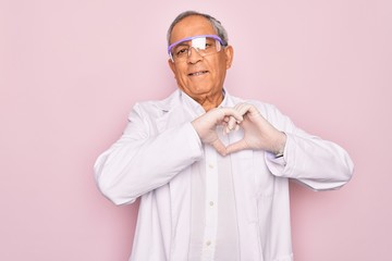 Senior grey-haired scientist man wearing glasses and coat over isolated pink background smiling in love showing heart symbol and shape with hands. Romantic concept.