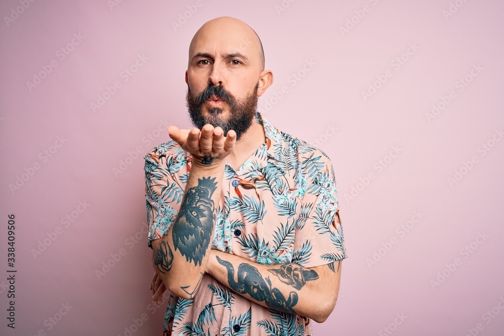 Poster handsome bald man with beard and tattoo wearing casual floral shirt over pink background looking at 