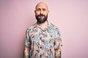 Handsome bald man with beard and tattoo wearing casual floral shirt over pink background puffing cheeks with funny face. Mouth inflated with air, crazy expression.