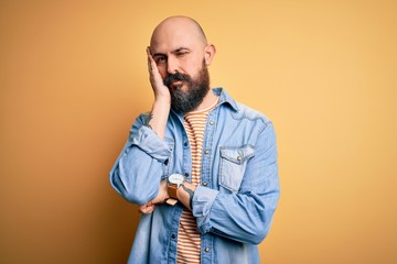 Handsome bald man with beard wearing casual denim jacket and striped t-shirt thinking looking tired and bored with depression problems with crossed arms.