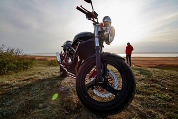 Fototapeta premium młody człowiek i motocykl o zachodzie słońca w pobliżu wody