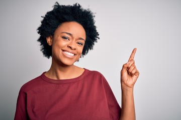 Young beautiful African American afro woman with curly hair wearing casual t-shirt standing with a big smile on face, pointing with hand and finger to the side looking at the camera.