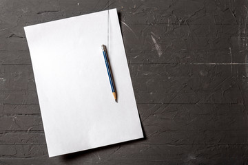 A sheet of paper and a pencil hang on a concrete wall. Background. Copy space.