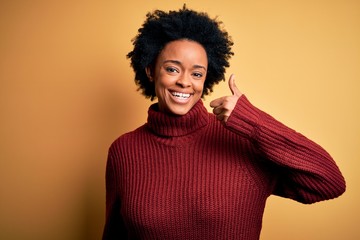 Obraz na płótnie Canvas Young beautiful African American afro woman with curly hair wearing casual turtleneck sweater doing happy thumbs up gesture with hand. Approving expression looking at the camera showing success.