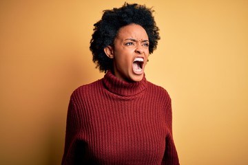 Fototapeta na wymiar Young beautiful African American afro woman with curly hair wearing casual turtleneck sweater angry and mad screaming frustrated and furious, shouting with anger. Rage and aggressive concept.