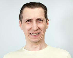 Fototapeta premium Zła twarz z uśmiechem mężczyzny, portret na szarym tle, seria emocji.