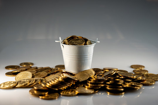 bucket full of coins surrounded by flat golden coins.