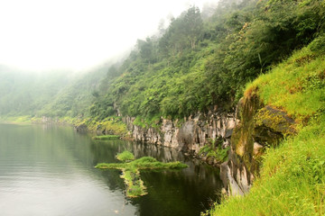 Fototapeta na wymiar photo of a foggy freshwater lake located in the mountains with a rock hill as one of the boundaries