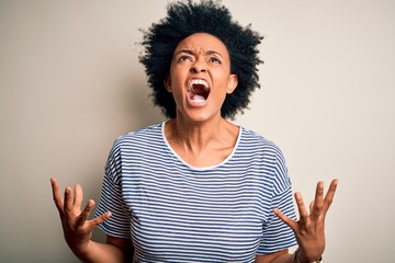 Young beautiful African American afro woman with curly hair wearing striped t-shirt crazy and mad shouting and yelling with aggressive expression and arms raised. Frustration concept.
