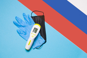 blue disposable medical glove, black face mask, infrared thermometer for non-contact temperature measurement on a white blue background, copy space