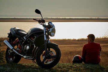  young man and motorcycle at sunset near the water © Руслан Сушко