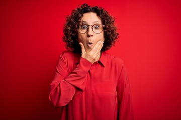 Fototapeta na wymiar Middle age beautiful curly hair woman wearing casual shirt and glasses over red background Looking fascinated with disbelief, surprise and amazed expression with hands on chin