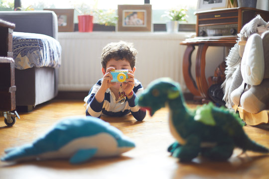 A little boy takes pictures with his camera of his toys.