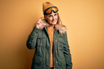 Middle age beautiful blonde skier woman wearing snow sportwear and ski goggles smiling and confident gesturing with hand doing small size sign with fingers looking and the camera. Measure concept.