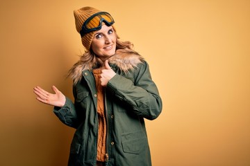 Middle age beautiful blonde skier woman wearing snow sportwear and ski goggles Showing palm hand and doing ok gesture with thumbs up, smiling happy and cheerful